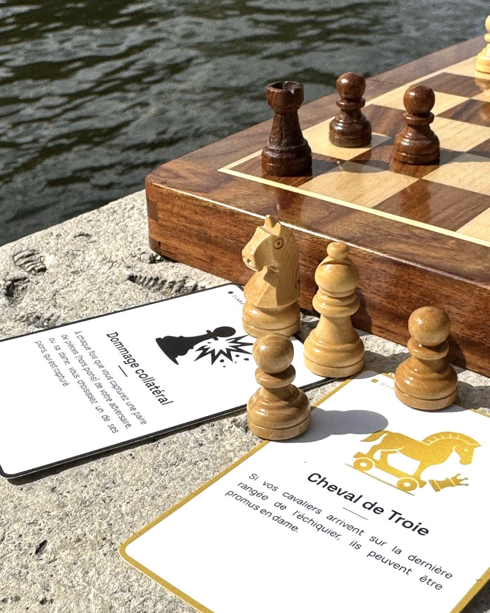 Pièces d’échecs en bois devant les cartes Dommage collatéral et Cheval de Troie