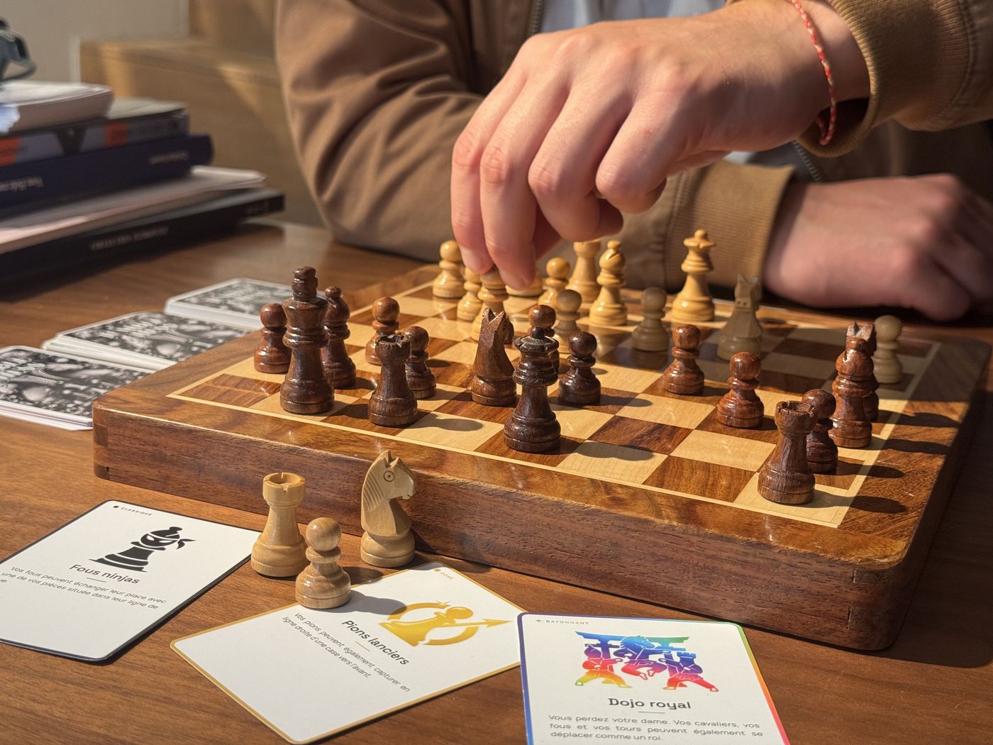 Un joueur déplace une pièce pendant une partie de Jumble Chess, cartes modificateurs posées à côté de l’échiquier